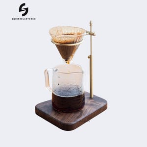 Op de afbeelding: Een walnotenhouten koffie-standaard met een messing druppelkoffiezetapparaat en een glazen karaf. Het koffiezetapparaat heeft een glazen filter en is gevuld met koffiedik. De karaf is gevuld met vers gezette koffie.