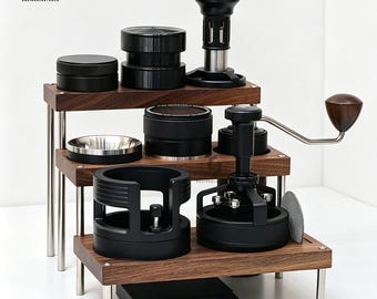May include: A three-tiered wooden display stand with silver metal legs holding various black espresso coffee accessories, including a tamper, a distributor, a portafilter funnel, and a hand grinder with a wooden knob, all arranged neatly.