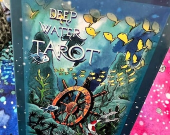 May include: A blue box with the words "Deep Water Tarot" and "Wheel of Fortune" on it. The box has a watercolor illustration of a wheel, fish, and seaweed.