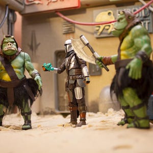 K&ouml;nnte beinhalten: Drei Actionfiguren, zwei gr&uuml;ne und eine silberne, stehen auf einer sandigen Oberfl&auml;che. Die gr&uuml;nen Figuren sind humanoid mit gro&szlig;en K&ouml;pfen und tragen braune Lederg&uuml;rtel und schwarze R&ouml;cke. Die silberne Figur tr&auml;gt einen Helm und eine R&uuml;stung und h&auml;lt eine silberne Axt. Die Figuren sind in einer Szene aus einem Science-Fiction-Film in Szene gesetzt.