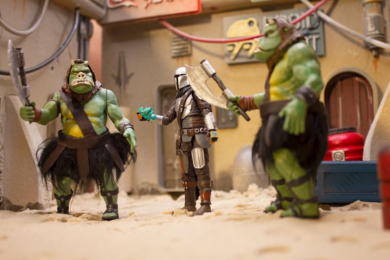 K&ouml;nnte beinhalten: Drei Actionfiguren, zwei gr&uuml;ne und eine silberne, stehen auf einer sandigen Oberfl&auml;che. Die gr&uuml;nen Figuren sind humanoid mit gro&szlig;en K&ouml;pfen und tragen braune Lederg&uuml;rtel und schwarze R&ouml;cke. Die silberne Figur tr&auml;gt einen Helm und eine R&uuml;stung und h&auml;lt eine silberne Axt. Die Figuren sind in einer Szene aus einem Science-Fiction-Film in Szene gesetzt.