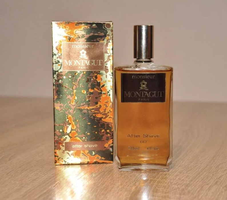 May include: A brown glass bottle of aftershave with a gold label that reads "Monsieur Montagut Paris" and "After Shave 60". The bottle is sitting on a wooden surface.