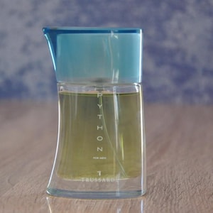 Peut inclure: Un flacon de parfum Trussardi Python Eau de Toilette en verre transparent. Le flacon est bleu et a une forme incurvée. Le flacon est étiqueté avec le nom "Python" et le nom de la marque "Trussardi".