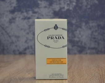 May include: A rectangular perfume box with the text "LES INFUSIONS DE PRADA MILANO" in black. Below, a rectangular orange label reads "INFUSION DE MANDARINE". The box is cream-colored and has a silver oval design. The bottle contains 3.3 fl oz.