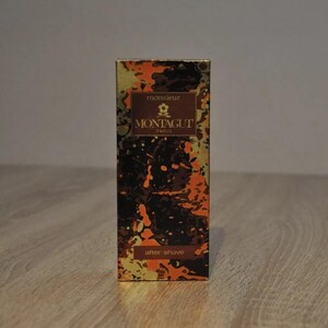 May include: A gold and orange box with a black and white abstract design. The box has the text "monsieur MONTAGUT PARIS" and "after shave" on it.