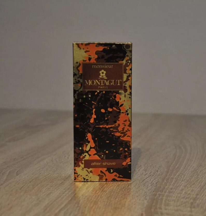 May include: A gold and orange box with a black and white abstract design. The box has the text "monsieur MONTAGUT PARIS" and "after shave" on it.