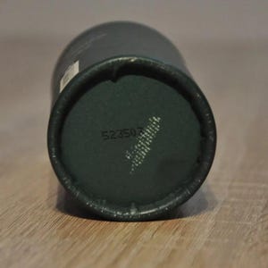 May include: Close-up of the bottom of a dark green cylindrical container with the number 523507 printed on it.