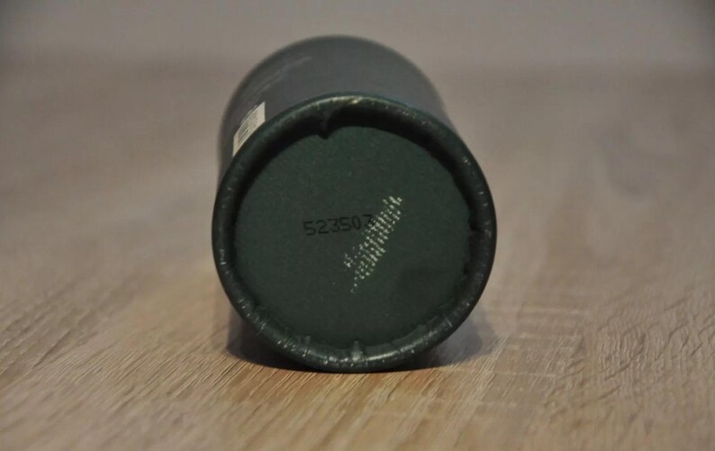 May include: Close-up of the bottom of a dark green cylindrical container with the number 523507 printed on it.