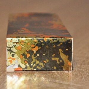 May include: A rectangular box with a black, gold, and orange patterned design. The box is made of cardboard and has a glossy finish.