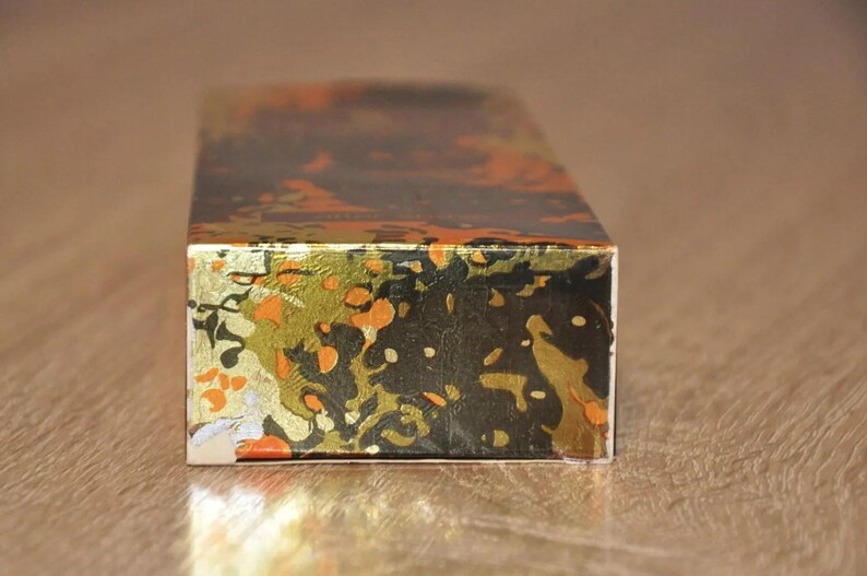 May include: A rectangular box with a black, gold, and orange patterned design. The box is made of cardboard and has a glossy finish.