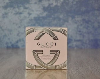 May include: A rectangular box of Gucci Bamboo Eau de Toilette. The box is light pink with silver accents and the Gucci logo. The text "GUCCI BAMBOO" is printed on the front. The box contains 75ml or 2.5 fl oz.