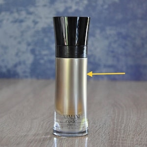 Puede incluir: Un frasco de perfume con tapa negra y cuerpo dorado metálico. El frasco tiene las palabras "Armani Code Absolu" impresas en la parte delantera. El frasco es cilíndrico y está sobre una superficie de madera.