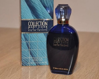 May include: A blue glass bottle of Mary Cohr Collection Eau de Toilette perfume with a gold cap and label. The bottle is sitting on a wooden surface next to a blue and gold box with the same text.