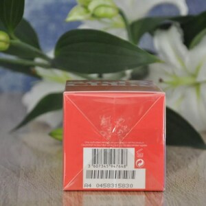 May include: A red product box with a barcode and text. The box is in front of white flowers and green leaves. The box has a brown top and a white label with the text "A4 0458315830".