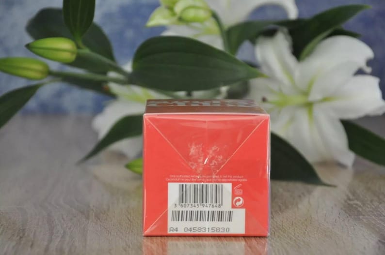 May include: A red product box with a barcode and text. The box is in front of white flowers and green leaves. The box has a brown top and a white label with the text "A4 0458315830".