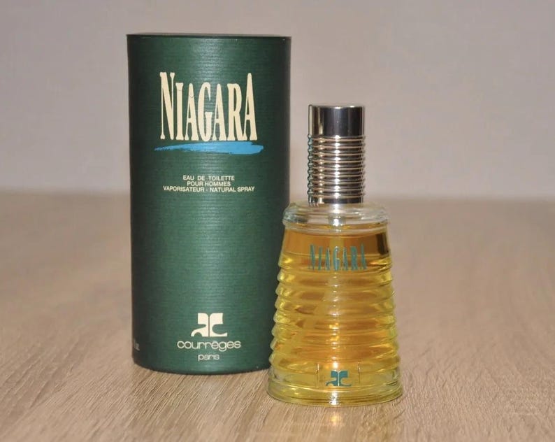 May include: A green box with the text "NIAGARA" in white letters and the text "COURREGES PARIS" in white letters. The box contains a clear glass bottle of perfume with a silver cap. The bottle has a textured design and the text "NIAGARA" in blue letters.