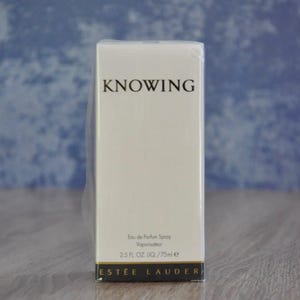 May include: An off-white rectangular box of Estée Lauder Knowing Eau de Parfum Spray. The box has the word "KNOWING" in black, with product details and brand name at the bottom. The box contains 75ml of perfume.