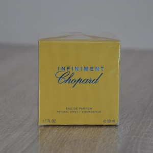 May include: A yellow perfume box with the words "INFINIMENT Chopard" in blue script. The box also includes the text "EAU DE PARFUM NATURAL SPRAY / VAPORISATEUR" and "1.7 FL OZ". The perfume bottle is 50 ml.
