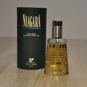 May include: A black and blue box with the text "NIAGARA" in white letters. The box contains a clear glass bottle of cologne with a silver cap. The bottle has a textured design and the text "NIAGARA" in gold letters. The cologne is by the brand "Courr&egrave;ges Paris".