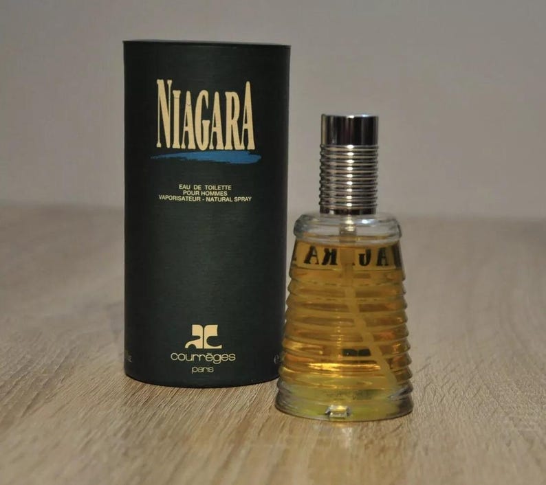 May include: A black and blue box with the text "NIAGARA" in white letters. The box contains a clear glass bottle of cologne with a silver cap. The bottle has a textured design and the text "NIAGARA" in gold letters. The cologne is by the brand "Courr&egrave;ges Paris".