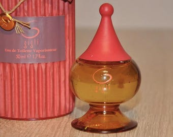May include: A small amber glass bottle of Gigli Eau de Toilette Vaporisateur, with a red cap and a gold label. The bottle is 50 ml or 1.7 fl oz.