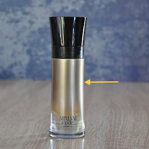 Puede incluir: Botella de perfume cilíndrica con tapón negro y cuerpo plateado. La botella tiene la inscripción "Armani Code Absolu". La botella está sobre una superficie de madera.