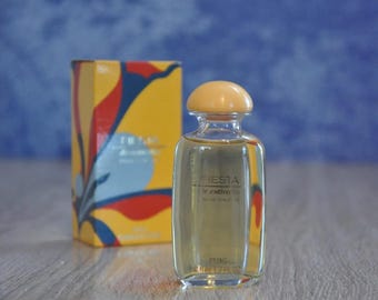 May include: A clear glass bottle of Fiesta Le Cotidiana Eau de Toilette perfume. The bottle has a yellow cap and a yellow label with the text "Fiesta Le Cotidiana Eau de Toilette" and "Pung 3.4 fl oz".