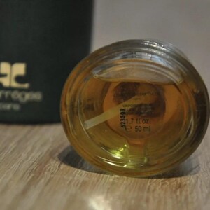 May include: Close-up of a clear glass bottle with a gold cap. The bottle contains a yellow liquid and has a label with the text "1.7 fl oz e 50 ml".