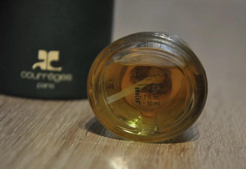 May include: Close-up of a clear glass bottle with a gold cap. The bottle contains a yellow liquid and has a label with the text "1.7 fl oz e 50 ml".
