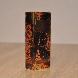 May include: A brown and gold aftershave bottle with a black and gold abstract design. The bottle is labeled "Original" and "BRUNI" with the text "after shave" on the bottom. The bottle is 125 ml or 4.2 fl oz.