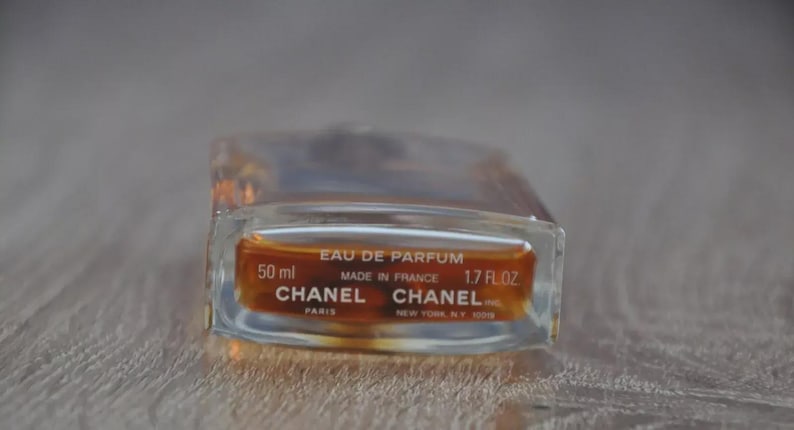 May include: A rectangular glass perfume bottle with a clear body and amber-colored liquid. The label reads "EAU DE PARFUM" and "CHANEL" with the volume of 50 ml and 1.7 fl oz. The bottle is made in France.