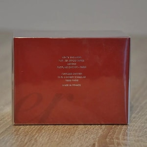 May include: Red rectangular box with white text detailing product information including 'Cartier', 'Paris', and 'Made in France'.  The box is primarily red with a subtle, embossed logo.  The packaging suggests a luxury perfume or cosmetic product.