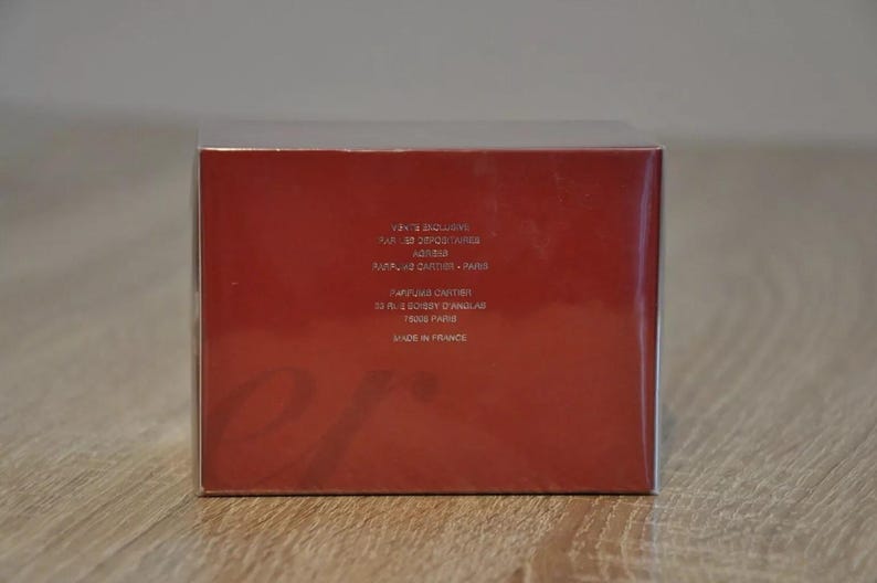 May include: Red rectangular box with white text detailing product information including 'Cartier', 'Paris', and 'Made in France'.  The box is primarily red with a subtle, embossed logo.  The packaging suggests a luxury perfume or cosmetic product.