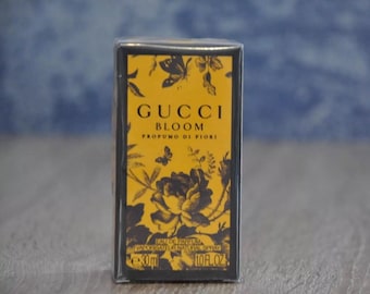 May include: A rectangular perfume box with a black border and a yellow front panel. The front panel features the words "GUCCI BLOOM PROFUMO DI FIORI" in white, along with floral and butterfly illustrations. The box also indicates a 30ml size and 1.0 fl oz.