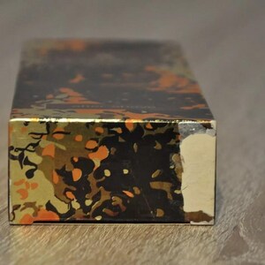 May include: A rectangular box with a gold and black abstract pattern. The box has a slightly damaged corner.