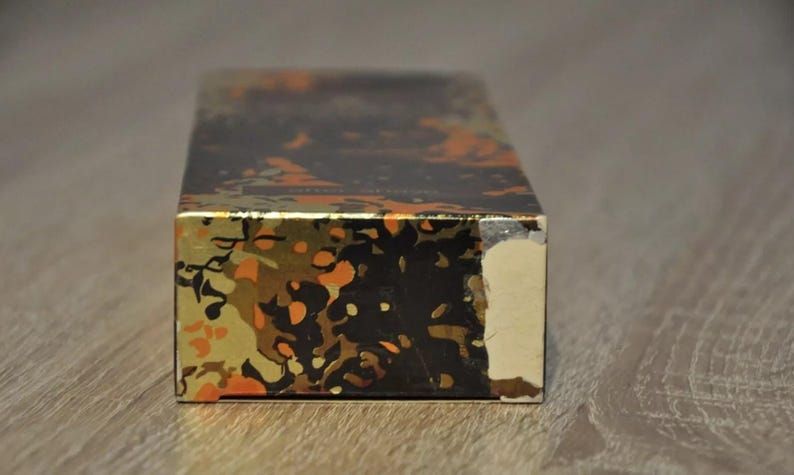 May include: A rectangular box with a gold and black abstract pattern. The box has a slightly damaged corner.