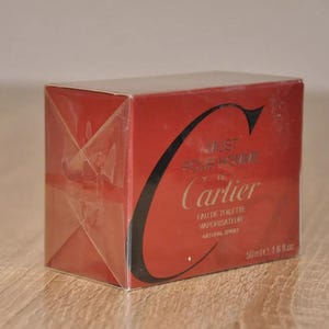 May include: A red Cartier Just For Her Eau de Toilette vaporisateur natural spray perfume box. The box features the Cartier logo and product details, including the volume (50ml e 1.6 fl.oz). The packaging is primarily red with black text and a gold-colored logo.