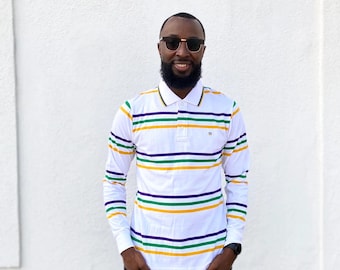 May include: A man wearing a white long-sleeved shirt with green, yellow, and purple stripes. The shirt has a collar and a button closure. He is wearing black trousers and sunglasses.