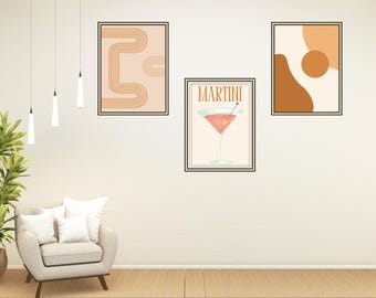 May include: Three framed prints on a white wall. The print on the left features a geometric design in orange and brown. The print in the center features a martini glass with the word "MARTINI" above it. The print on the right features a brown and orange abstract design.