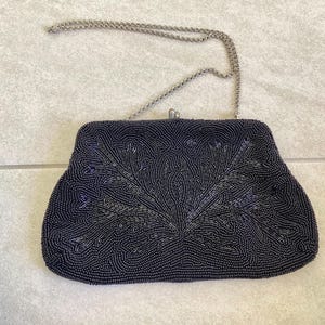 Pode incluir: Uma bolsa de noite azul escuro com contas e uma corrente prateada. A bolsa apresenta um design floral em contas mais claras. O fecho é prateado. Estilo vintage.