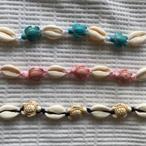 May include: Three bracelets featuring white seashells and turtle charms. The top bracelet has turquoise turtles, the middle bracelet has pink turtles, and the bottom bracelet has beige turtles.