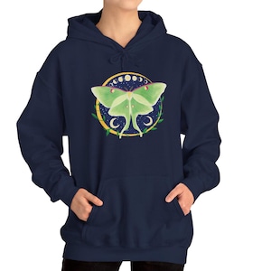 May include: A navy blue hoodie with a green luna moth design. The moth is surrounded by a circle of yellow crescent moons and stars on a dark blue background.