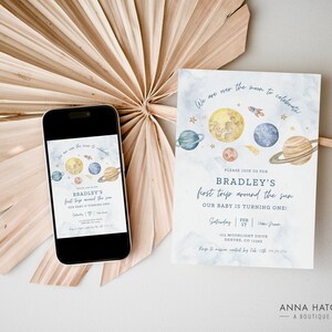 Puede incluir: Una tarjeta de invitaci&oacute;n azul y blanca con una ilustraci&oacute;n de acuarela de planetas y estrellas. El texto en la tarjeta dice "We are over the moon to celebrate Bradley's first trip around the sun. Our baby is turning one!"