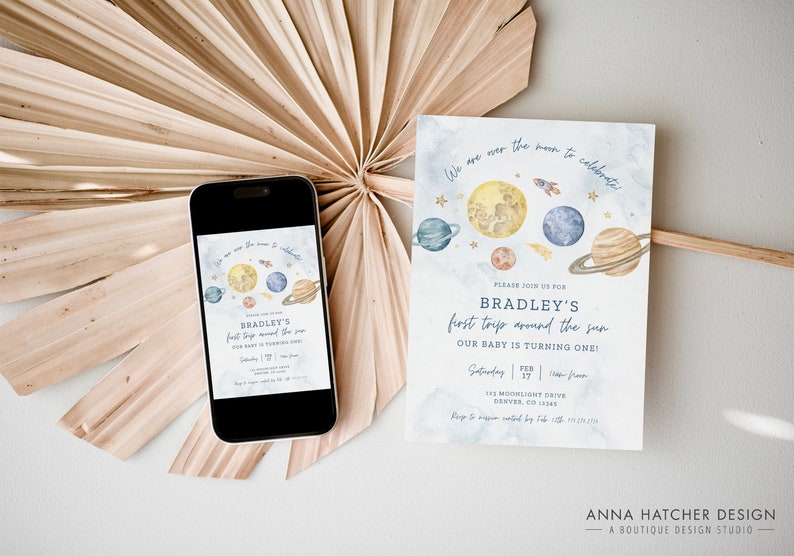 Puede incluir: Una tarjeta de invitaci&oacute;n azul y blanca con una ilustraci&oacute;n de acuarela de planetas y estrellas. El texto en la tarjeta dice "We are over the moon to celebrate Bradley's first trip around the sun. Our baby is turning one!"