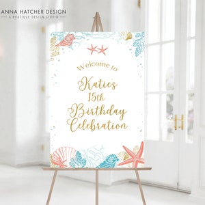 May include: A welcome sign on an easel with a beach theme. The sign reads "Welcome to Katie's 15th Birthday Celebration" in gold script. The sign is decorated with illustrations of seashells, starfish, and coral in shades of blue, coral, and gold.