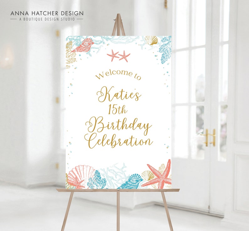 May include: A welcome sign on an easel with a beach theme. The sign reads "Welcome to Katie's 15th Birthday Celebration" in gold script. The sign is decorated with illustrations of seashells, starfish, and coral in shades of blue, coral, and gold.