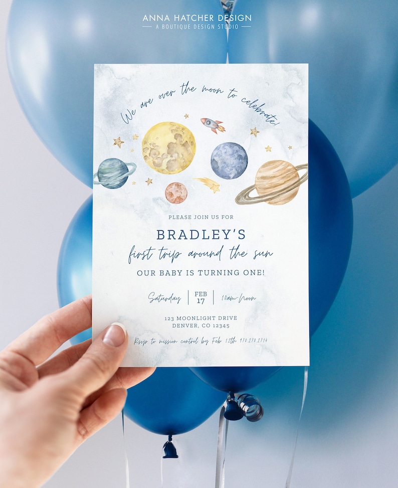 Puede incluir: Una tarjeta de invitaci&oacute;n azul y blanca con una ilustraci&oacute;n de acuarela de planetas y un cohete. El texto dice "We are over the moon to celebrate!" y "Bradley's first trip around the sun. Our baby is turning one!" La invitaci&oacute;n incluye la fecha, la hora y la ubicaci&oacute;n del evento.