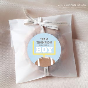 Może przedstawiać: Niebieska i biała etykieta na prezent z okazji baby shower z grafiką piłki nożnej i strefy końcowej. Etykieta zawiera napis "Team Thompson is having a Boy".