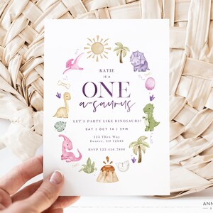 Puede incluir: Una invitaci&oacute;n a una fiesta de cumplea&ntilde;os de primer a&ntilde;o con tem&aacute;tica de dinosaurios en morado y verde con el texto "Katie is a One-a-saurus! Let's party like dinosaurs!" y detalles de la fiesta, incluyendo la fecha, la hora y la ubicaci&oacute;n.