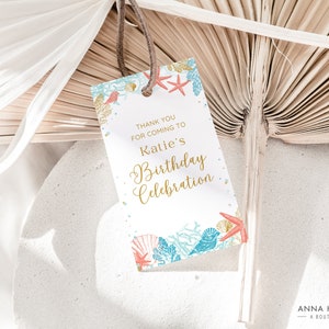 May include: A white gift tag with a beach theme, featuring text that reads "Thank you for coming to Katie's Birthday Celebration." The tag is decorated with illustrations of seashells, coral, and starfish in gold, teal, and red.